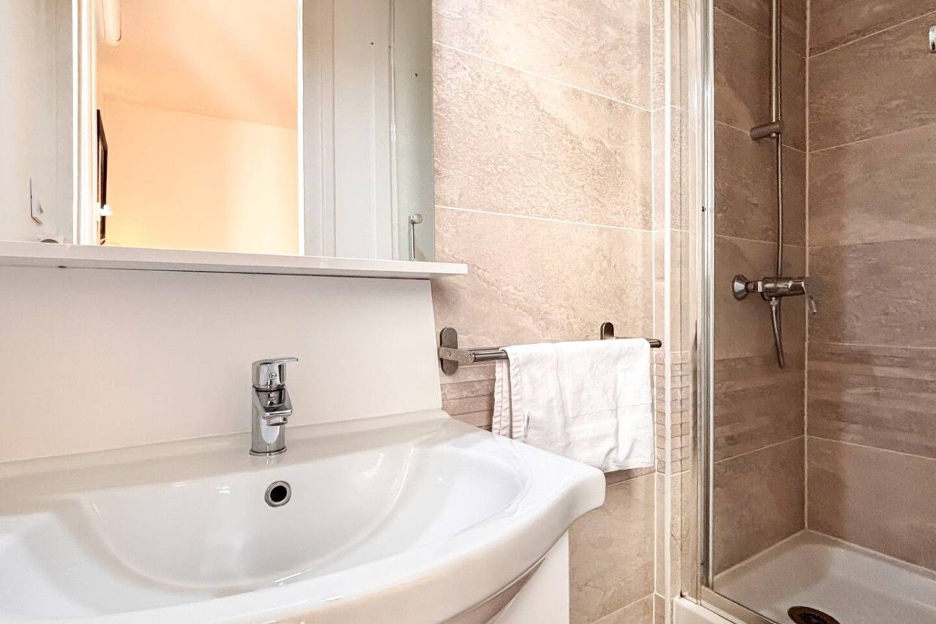 Une salle de bain équipée d’un lavabo, d’un miroir, d’un porte-serviettes et d’une douche.