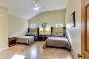 Quarto de hotel com duas camas de solteiro, ventilador de teto, janela com vista e uma porta.