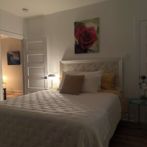 A bedroom with a large bed, a nightstand, a lamp, and a painting of a rose on the wall. - THE ARTFUL TIDE - Unit B/Beautiful 2 BR/1BA Mansion Suite (Atlantic City)