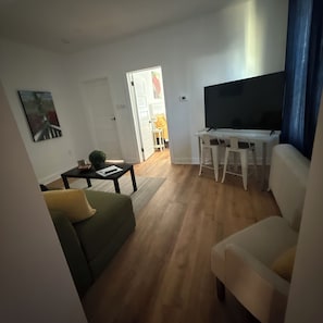 A living room with a sofa, a coffee table, a TV, and a dining area with chairs. - THE ARTFUL TIDE - Unit B/Beautiful 2 BR/1BA Mansion Suite (Atlantic City)