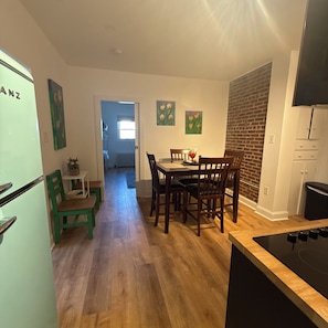 A kitchen with wooden flooring, a dining table with chairs, a refrigerator, and a brick wall. - THE ARTFUL TIDE - Unit B/Beautiful 2 BR/1BA Mansion Suite (Atlantic City)