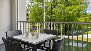 Een balkon met rieten meubels en een tafel, met uitzicht op een groen landschap met bomen en een waterpartij.
