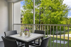 Ein Balkon mit Korbmöbeln und einem Tisch, mit Blick auf eine grüne Landschaft mit Bäumen und einem Gewässer.