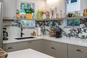 Eine moderne Küche mit Marmorfliesenspiegel, einer Kaffeemaschine und dekorativen Gegenständen auf Regalen.