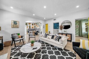 A modern living room with a sofa, coffee table, and chairs, a dining area with a table and chairs, and a kitchen visible through an archway. - Downtown West Palm Beach Posh Pinneapple (West Palm Beach)