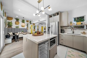 A modern kitchen with a central island, stainless steel appliances, and a dining area with a patterned wall. - Downtown West Palm Beach Posh Pinneapple (West Palm Beach)
