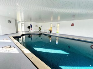 An indoor swimming pool with a tiled floor, benches along the walls, and a clock on the wall. - Cottage Sleeps 4 Indoor Pool, Fishing Lake, Pets (Beaworthy)