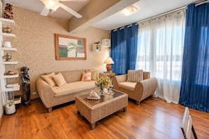 Ein Wohnzimmer mit Sofa, Sessel und Couchtisch, Holzboden und Deckenventilator.