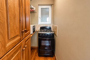 A compact kitchen with a stove, oven, and wooden cabinets. - Central Sosua 1BR , Balcony , Hard Rock Perks (San Felipe de Puerto Plta)