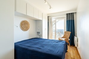 Ein Schlafzimmer mit Bett, einem Sessel, einem Fenster mit Vorhängen und Blick auf die Stadt.