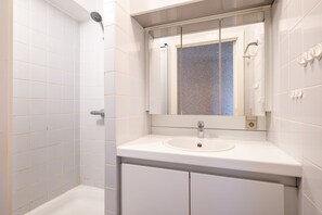 Ein Badezimmer mit weißen Fliesen, einem weißen Waschbecken, einem Spiegel und einer Dusche.