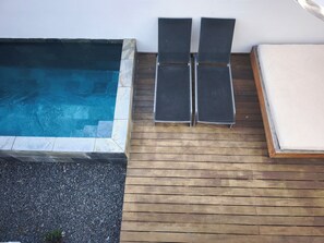 Ett trädäck med en pool, två solstolar och en madrass.