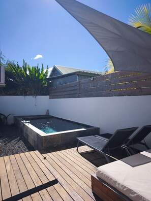 A wooden deck with a hot tub, lounge chairs, and a shaded area with a white canopy.