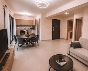 A modern living room with a sofa, a dining table with chairs, a coffee table, and a TV on a stand. - Luxury Apartment and wirlpool over athen/Kesariani (Kesariani)