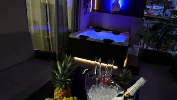 Ein Zimmer mit großem Fenster, einer Minibar mit einer Champagnerflasche und einer Obstschale mit Trauben und Ananas.
