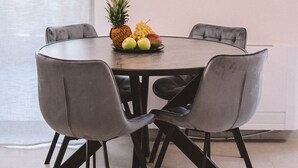 Een eetgedeelte met een ronde tafel, vier grijze stoelen en een schaal fruit op de tafel.