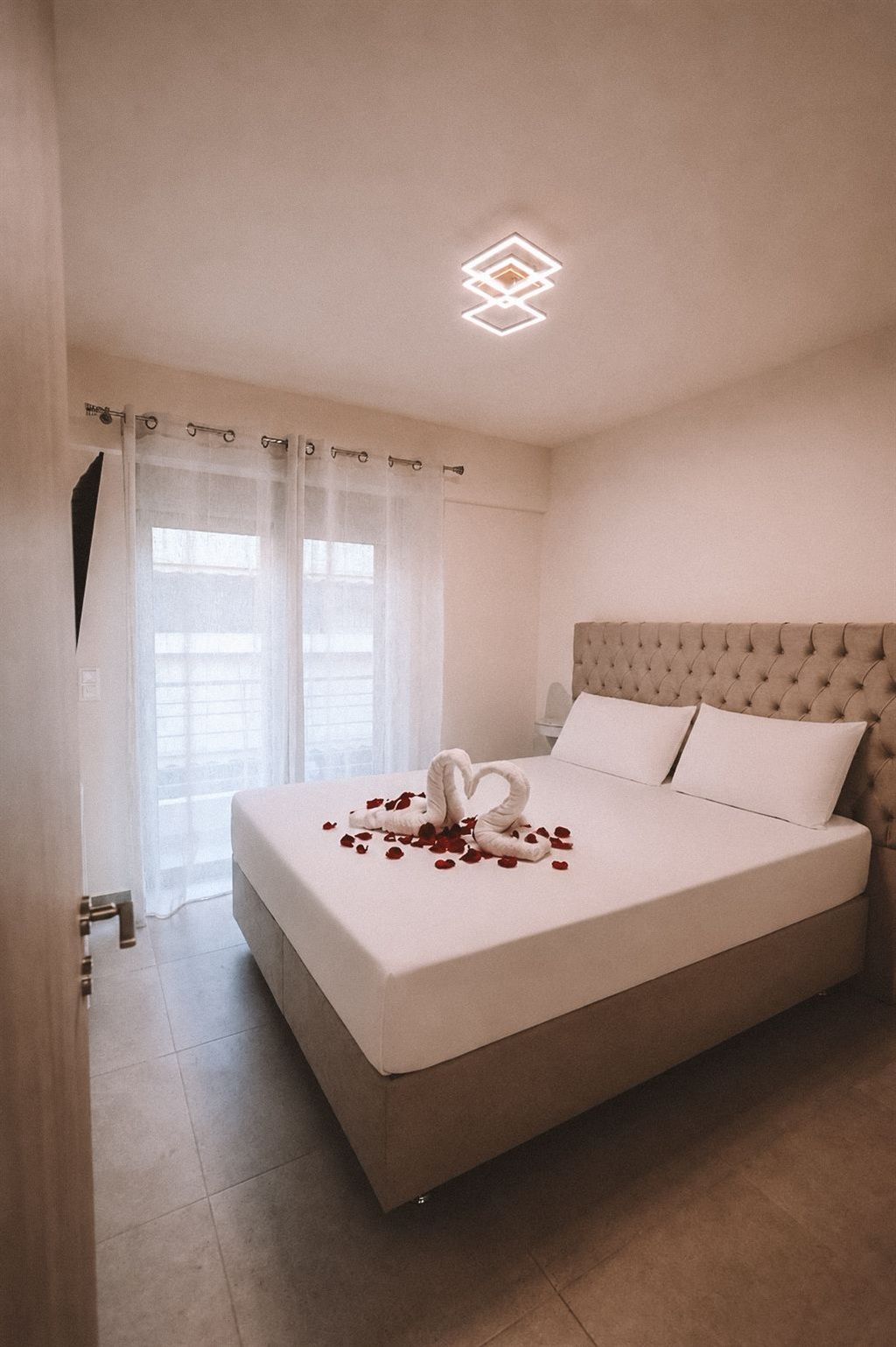 Ein Hotelzimmer mit einem großen Bett, einem gepolsterten Kopfteil und einem dekorativen Schwan aus Rosenblättern auf dem Bett.