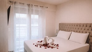 Een hotelkamer met een groot bed, een gestapeld hoofdeinde en een decoratieve zwaan van rozenblaadjes op het bed.