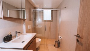 Een moderne badkamer met een douchecabine van glas, een witte wastafel en een toilet.