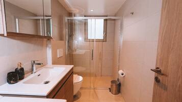 Ein modernes Badezimmer mit einer gläsernen Dusche, einem weißen Waschbecken und einer Toilette.