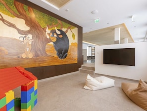 Ein modernes Interieur mit Wandgemälde, einer Spielecke, einer Sitzecke und einem Flachbildfernseher.