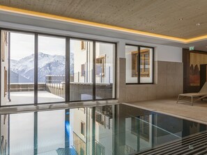 Ein moderner Poolbereich im Innenbereich mit großen Fenstern, einer Glasbarriere und Blick auf Berge.