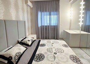 A bedroom with a bed, bedside tables, a vanity with lights, and a window with curtains. - AeroZen Studio (Gouvernorat de l'Ariana)