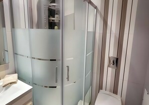 Un baño moderno con cabina de ducha de vidrio, inodoro y tocador con espejo.