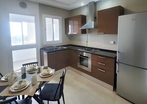 Eine moderne Küche mit Gasherd, Backofen und einem Edelstahlkühlschrank. Ein Esstisch ist mit Tellern und Tassen gedeckt.