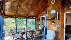 Eine Holzhütte mit Essbereich, Liegestuhl und Blick auf den Wald.