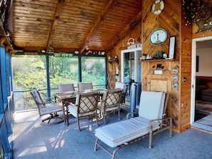 Une cabane en bois comprenant un coin repas, un fauteuil et une vue sur la forêt.