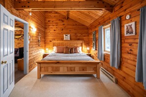 Ett sovrum i en stuga med träpanel, en säng, sänglampor, en klocka och ett fönster med gardiner.