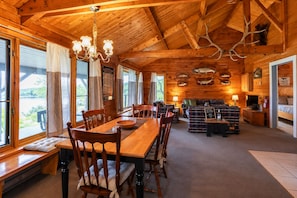 A wooden cabin interior with a dining area, sofas, and a fireplace.