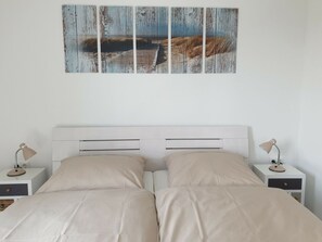 A bedroom with a white headboard, two bedside tables with lamps, and a large painting above the bed. - 48.5.s Waterkant (Wangerland)