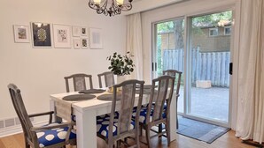 Uma sala de jantar com mesa branca, cadeiras cinzentas com almofadas azuis, um candelabro e quadros nas paredes.