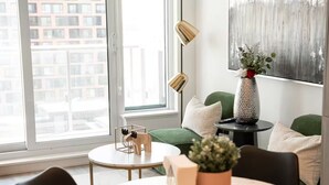 Uma sala de estar moderna com uma janela ampla, uma mesa redonda, um sofá verde e um vaso decorativo.
