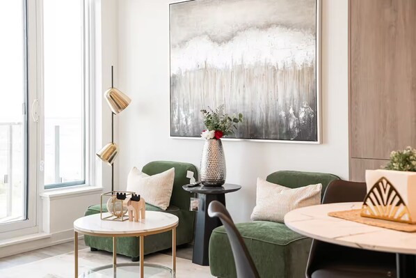 En moderne stue med en grøn sofa, et rundt sofabord og et minimalistisk billede på væggen.