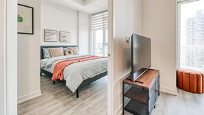 Um quarto moderno com uma cama, uma televisão sobre um suporte e uma janela com persianas.