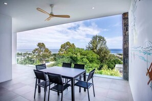 A modern dining area with a table and chairs, a ceiling fan, and a view of the ocean and greenery. - Sunset and Sea Views - Two Bed Apt Central Tamarin (Black River)