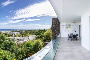 Un balcone moderno con ringhiera in vetro che si affaccia su un paesaggio rigoglioso e vista sull'oceano.