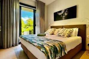 Ein Schlafzimmer mit einem großen Bett, Blick ins Grüne durch eine Schiebetür und einem Bild an der Wand.