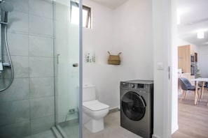 Une salle de bain compacte avec une douche à parois de verre, des toilettes et un lave-linge à chargement frontal.
