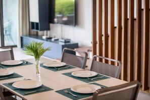 A dining area with a table set for six, including plates, cutlery, and a small plant centerpiece. - Luxurious Seafront Apartment with Pools (Grande Riviere Noire)