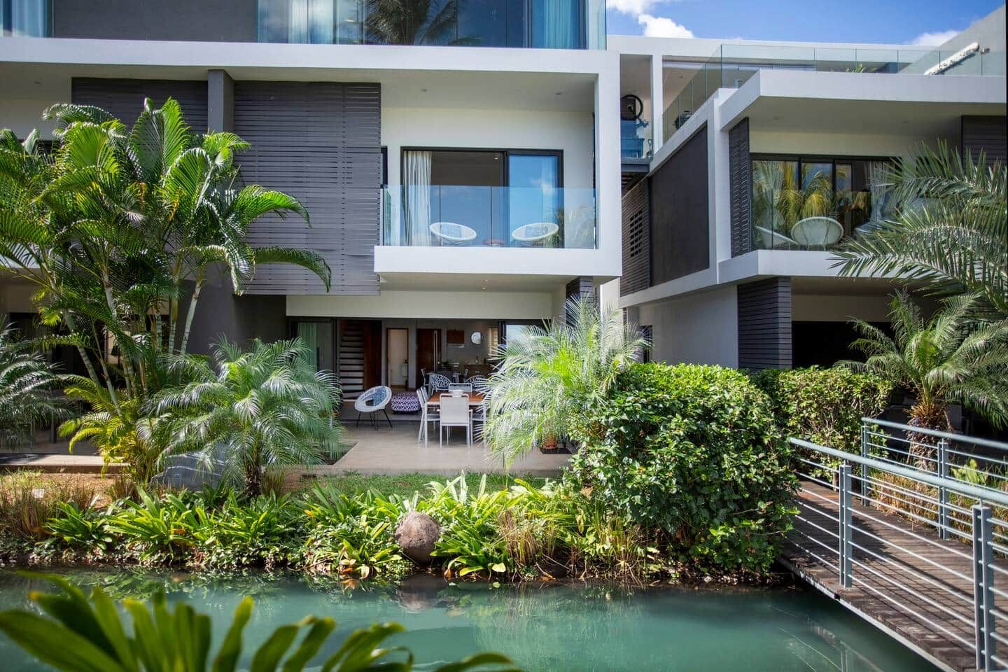 A modern two-story house with a pool, outdoor furniture, and lush greenery.