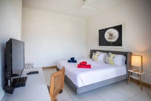 A hotel room with a bed, a desk with a computer, a chair, a TV, and a lamp. - Luxurious Seafront Apartment with Pools (Grande Riviere Noire)