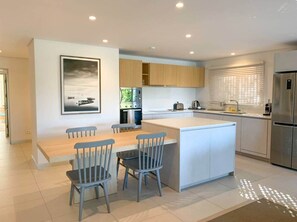 A modern kitchen with a central island, wooden cabinets, and a dining area with chairs. - Luxury Waterfront Apartment with Pools (Grande Riviere Noire)