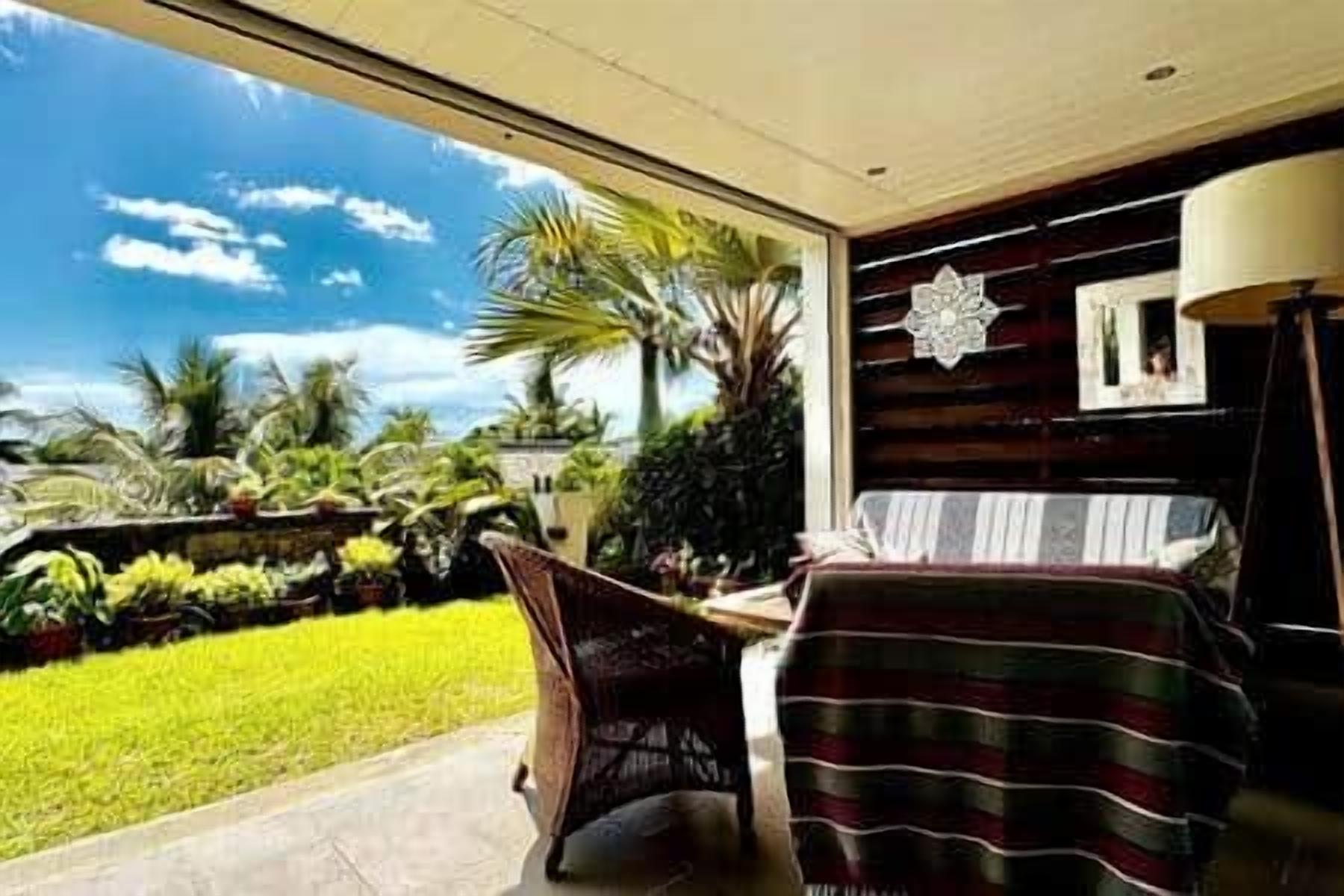A room with a view of a lush garden, a bed with a striped blanket, and a chair.