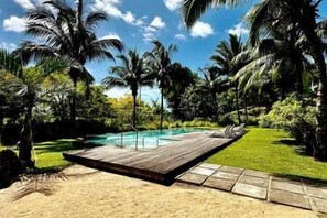 A wooden deck with a pool, surrounded by palm trees and greenery. - 2-bedroom apartment in Tamarin, shared pool and parking (Tamarin)