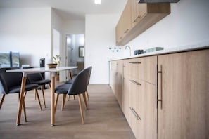 A modern kitchen with wooden cabinets, a white countertop, and a dining area with a table and chairs. - Modern Flat in Heart of Tamarin (Rivière Noire District)