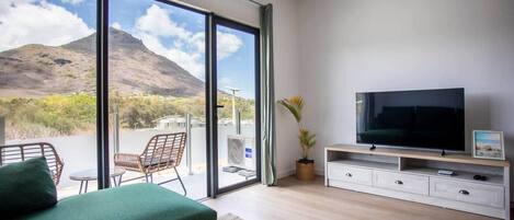 A modern living room with a large TV, a sofa, and a view of a mountain through large sliding doors.